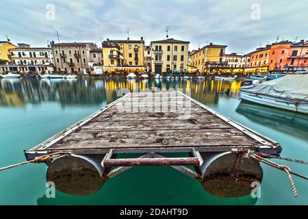 Vue panoramique de la plate-forme dans le canal du lac avec cygne, bateau et maisons et hôtel en arrière-plan pendant l'heure bleue, Peschiera del Garda, Vérone, Italie Banque D'Images