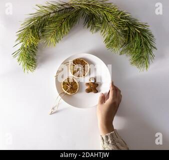 La main d'une femme dans un pull tient une assiette de bonbons de Noël. Biscuits sous forme d'homme dans un masque et tranches d'orange séchées à la cannelle. Banque D'Images