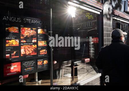 Un Londoner passe devant le menu éclairé d'Angus Steakhouse, qui est maintenant fermé pendant le deuxième confinement de la deuxième vague de la pandémie du coronavirus, le 6 novembre 2020, à Londres, en Angleterre. Ce dernier verrouillage du gouvernement durera 4 semaines au moins jusqu'au 2 décembre, lorsque seules les entreprises fournissant des services essentiels et dans le cas des restaurants, les plats à emporter seront autorisés à négocier. Banque D'Images