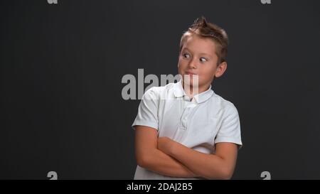 Le petit garçon caucasien de 10 ans regarde loin dans la surprise. L'enfant avec ses bras pliés pose sur fond noir. Concept surprise Banque D'Images