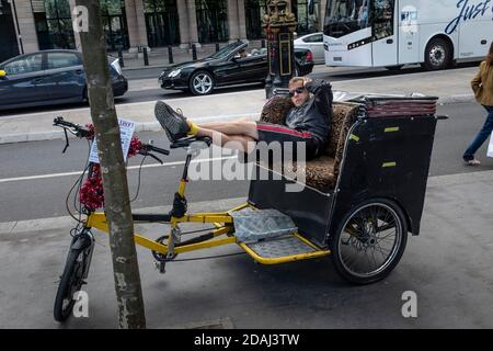 Un rider en pousse-pousse à vélo se détend entre les manèges, Londres. Banque D'Images