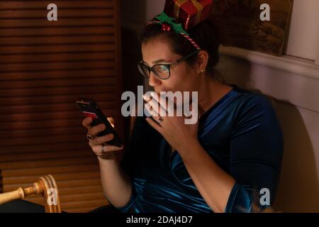 Émerveillement jeune femme avec un décor de cheveux de noël regardant dans son téléphone à noël. Banque D'Images