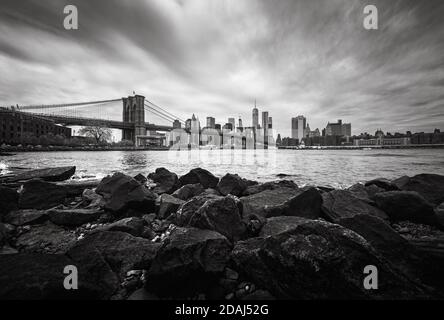 NEW YORK, États-Unis - 29 avril 2016 : image en noir et blanc de l'horizon de Manhattan avec le pont de Brooklyn. Rochers et pierres sur la rive de la rivière est. Manhat Banque D'Images