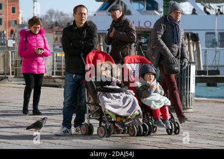 Un homme asiatique se tient avec ses enfants en fauteuil roulant La promenade centrale de Riva degli Schiavoni de Venise contre la toile de fond d'un bateau de croisière Banque D'Images