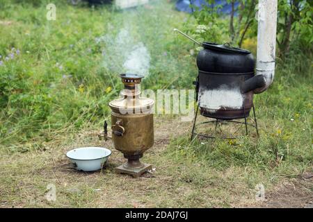 Le samovar et le poêle avec la chaudière pour la nourriture se tiennent sur l'herbe. Banque D'Images