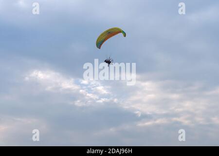 Un parapente motorisé en tandem vole dans le ciel nuageux de la soirée avec deux personnes. Banque D'Images