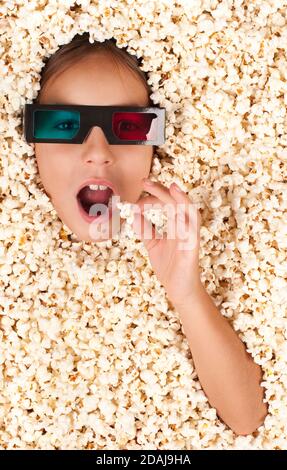 petite fille enterrée dans du pop-corn portant des lunettes 3d Banque D'Images