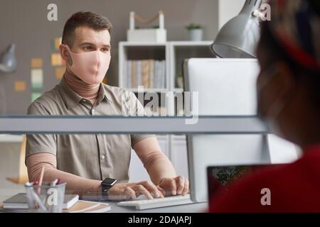 Jeune homme en masque de protection travaillant sur son lieu de travail à bureau Banque D'Images