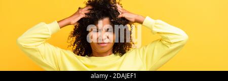 femme afro-américaine avec les yeux fermés fixant les cheveux bouclés sur le jaune, bannière Banque D'Images