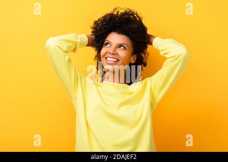 bonne femme afro-américaine regardant loin tout en fixant les cheveux bouclés sur jaune Banque D'Images