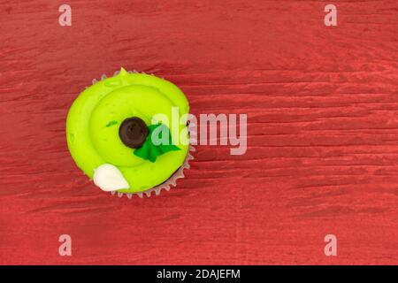 Vue de dessus d'un cupcake vert aux couleurs vives dépoli sur un fond de bois peint en rouge. Banque D'Images