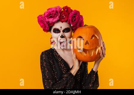 Effrayante jeune fille dans le maquillage halloween posant avec la citrouille isolée sur fond jaune Banque D'Images