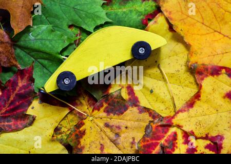 Voiture jouet en bois jaune sur des feuilles de couleur automnale Banque D'Images