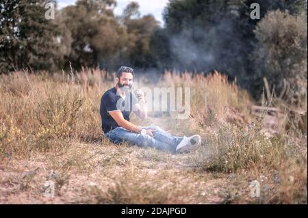 Style homme de vape barbu avec cigarette électronique dans la nature. Non-fumeurs. Banque D'Images