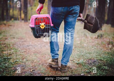 Homme toujours en forêt transportant une boîte de transport à l'intérieur avec un animal mort et une pelle pour enterrer un animal dans le bois. Perte d'animal en automne. Le mâle va faire un Banque D'Images