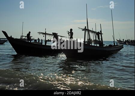 Les silhouettes des pêcheurs birmans ont préparé leurs bateaux de pêche pour un Nuits de pêche au coucher du soleil sur la plage de Ngapali Myanmar Banque D'Images