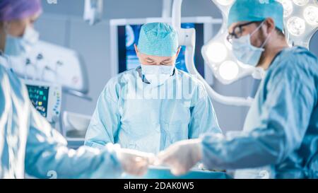 Tourné dans la salle d'opération, l'assistant remet les instruments aux chirurgiens pendant le fonctionnement. Les chirurgiens effectuent l'opération. Médecins professionnels Banque D'Images