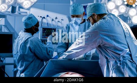 Équipe diversifiée de chirurgiens professionnels effectuant une chirurgie invasive sur un patient dans la salle d'opération de l'hôpital. L'infirmière remet les instruments au chirurgien Banque D'Images