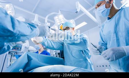 Prise de vue à angle bas d'une équipe diversifiée de chirurgiens professionnels effectuant une chirurgie invasive sur un patient dans la salle d'opération de l'hôpital. Les chirurgiens utilisent Banque D'Images