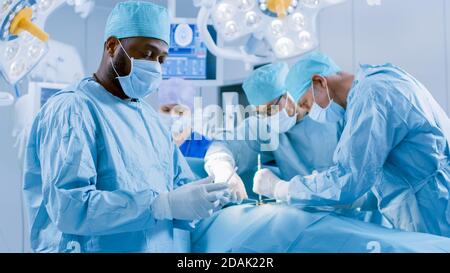 Chirurgien professionnel debout dans le masque chirurgical bras croisés. En arrière-plan salle d'opération de l'hôpital moderne avec chirurgie en cours. Banque D'Images