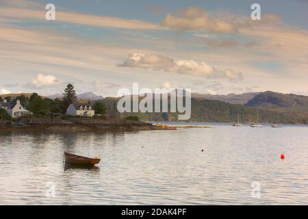 Une scène paisible à Plockton, Wester Ross. Un bateau à rames en bois s'embarque sur la marée descendante avec des chalets peints en blanc sur le rivage. Banque D'Images