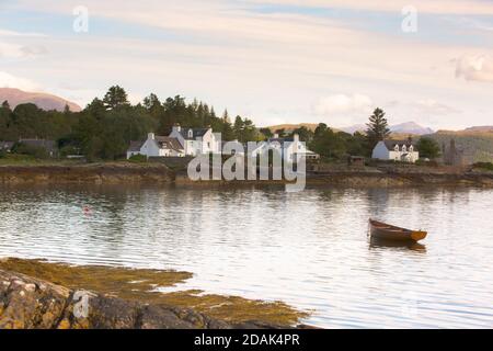 Une scène paisible à Plockton, Wester Ross. Un bateau à rames en bois s'embarque sur la marée descendante avec des chalets peints en blanc sur le rivage. Banque D'Images