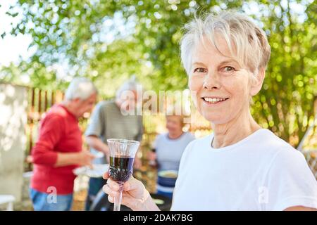 Femme âgée souriante avec un verre de vin rouge à un barbecue d'été Banque D'Images