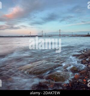 Une côte de la baie de mer avec des pierres au coucher du soleil Près du pont New Queensferry Crossing en Écosse Banque D'Images