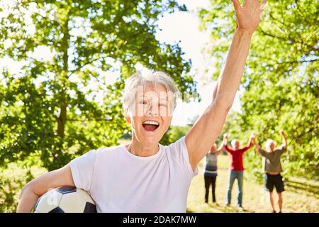 Encourager une femme de haut niveau jouant au football avec des amis dans le parc en été Banque D'Images