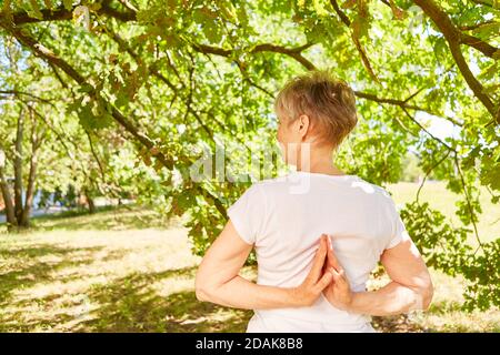 Femme âgée dans une posture de prière faisant du yoga avec les mains derrière elle dans la nature Banque D'Images