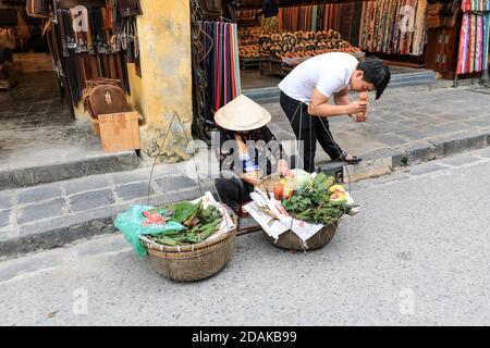 Un vendeur de nourriture de rue vendant des fruits et des légumes et un client mettant de la sauce sur la nourriture qu'il vient d'acheter, Hoi an, Vietnam, Asie Banque D'Images