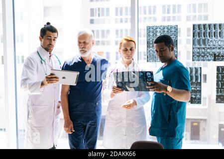 Un groupe de médecins multi-ethniques discute de l'histoire de la maladie du patient en utilisant l'IRM et le comprimé. Banque D'Images