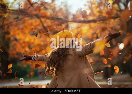 Bonjour automne. Vue de derrière la femme d'âge moyen en manteau beige et chapeau orange se réjouissant dehors sur le parc de la ville en automne. Banque D'Images