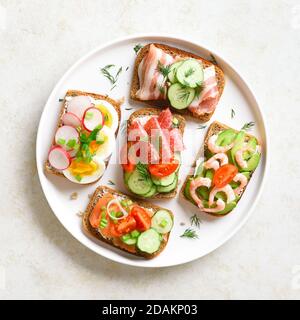 Différents sandwichs avec viande, légumes, fruits de mer. Assortiment de sandwichs ouverts sur plaque sur fond de pierre légère. En-cas savoureux et sains. Vue de dessus, f Banque D'Images