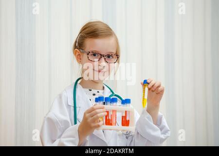 Une petite fille dans un smock de docteur examine les tubes à essai avec des tests. Jeu médical éducatif. Banque D'Images