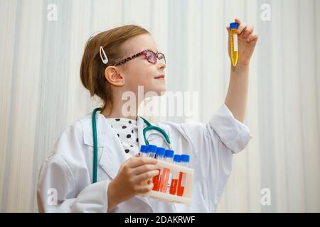 Une petite fille dans un smock de docteur examine les tubes à essai avec des tests. Jeu médical éducatif. Banque D'Images