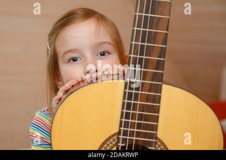 Une petite fille sort de derrière un étui de guitare à la maison. Banque D'Images