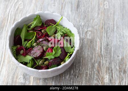 Salade de betteraves avec oignon rouge cuit, câpres, cresson, légumes verts et sauce vinaigrette. Nourriture saine végétalienne. Dans un bol bleu sur une table en bois Banque D'Images
