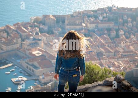 Brunette portant un Jean bleu et un haut bleu vu de derrière sur la montagne au-dessus de la ville de Dubrovnik, ville étonnante vue en arrière-plan wi Banque D'Images