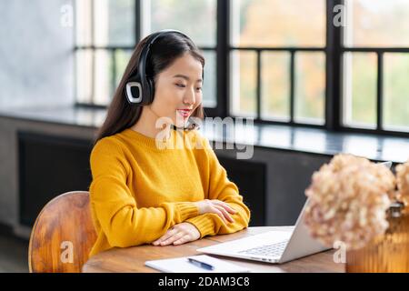 Femme asiatique dans un micro-casque parlant par conférence téléphonique et vidéo discutez sur un ordinateur portable au bureau Banque D'Images