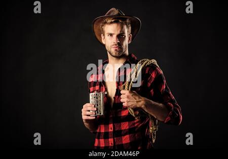 Toujours boire en amont du troupeau. Homme de style vintage. Cow-boy rétro de l'Ouest sauvage. Cowboy avec corde de lasso. WESTERN. Wild West rodeo. Man in Hat fond noir. Man checked shirt sur ranch. Banque D'Images