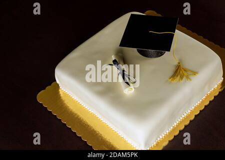 Gâteau blanc de remise de diplôme avec chapeau sur le dessus et décor de diplôme. Banque D'Images