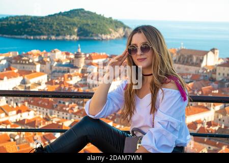 Un influenceur de brunette attrayant assis sur les murs de la ville de Dubrovnik, posant pour une photo verticale pour les médias sociaux. Toits de la vieille ville dans le b Banque D'Images