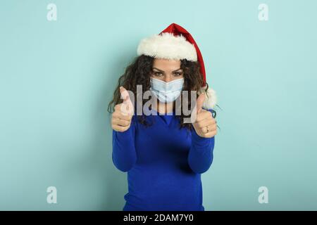 Fille avec chapeau de noël est optimiste au sujet de la défaite de covid 19 coronavirus. Fond cyan. Banque D'Images