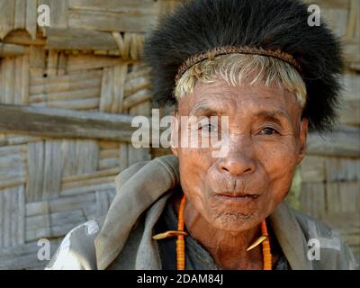 Ancien retraité Indien du Nord-est Konyak Naga guerrier et chasseur de tête avec chapeau de fourrure traditionnel mâche paan et pose pour la caméra. Banque D'Images