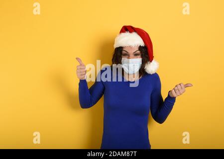 Fille avec chapeau de noël est optimiste au sujet de la défaite de covid 19 coronavirus. Fond cyan. Banque D'Images