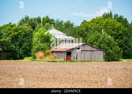 Une grange en bois ou un bâtiment agricole en ruine, et une ancienne ferme abandonnée dans la campagne à côté d'un champ labouré dans le Kansas, États-Unis. Banque D'Images