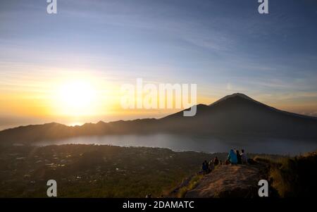 Randonneurs se rassemblant sur le bord de la caldeira du mont Batur pour le lever du soleil, Bali, Indonésie. Lac Batur ci-dessous. Banque D'Images