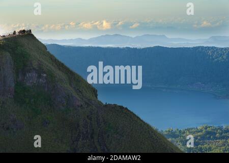 Les randonneurs se rassemblent sur le sommet de la caldeira du mont Batur pour le lever du soleil, Bali, Indonésie. Lac Batur ci-dessous. Banque D'Images