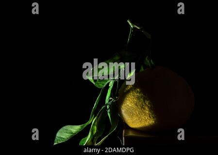 Une mandarine avec des feuilles vertes sur une table en bois devant l'arrière-plan noir, isolée, proche, espace pour le texte ou l'image de logo Banque D'Images